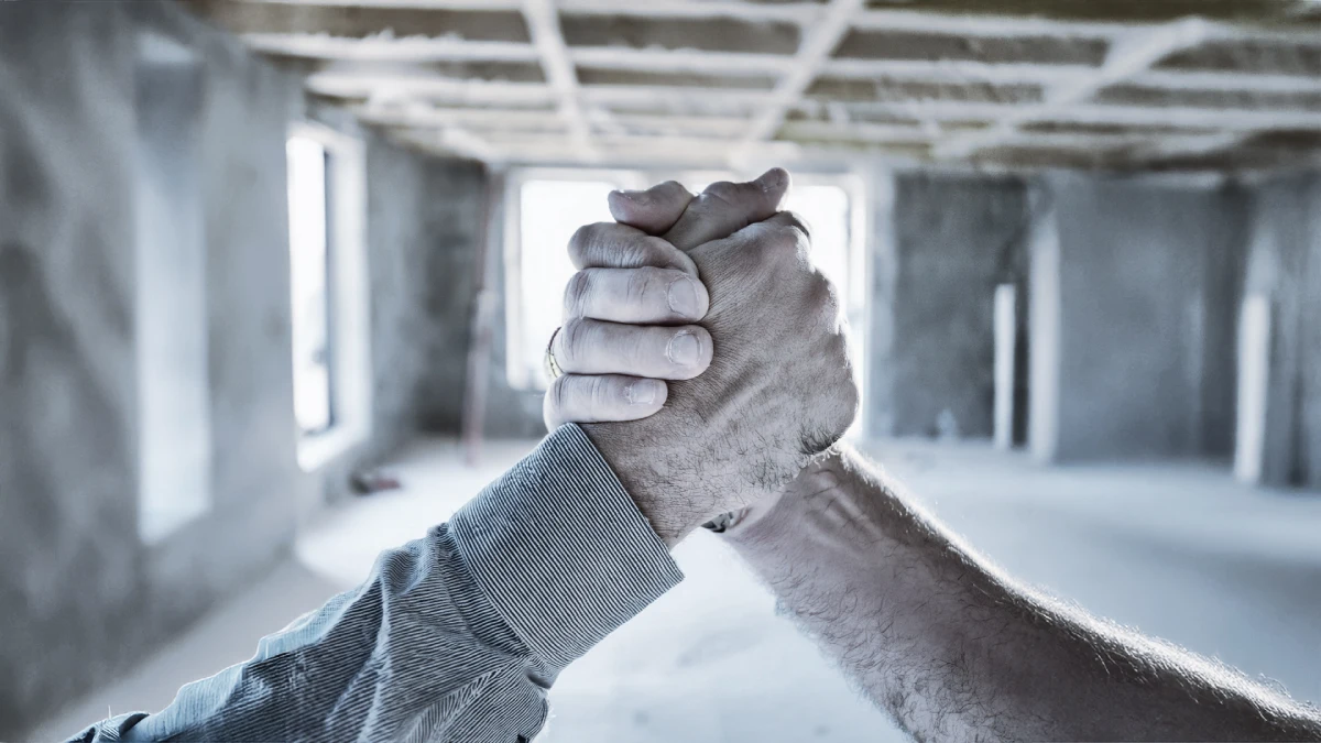 Stretta di mano tra due operai in un cantiere Mae Home