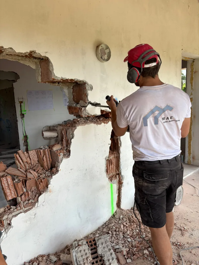 In cantiere: un operaio di spalle, con la maglia Mae Home, demolisce una parete